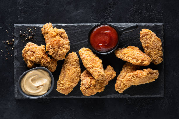 Spicy deep fried chicken wings with sauces on black slate Spicy deep fried chicken wings with sauces served on black slate background, top view. Junk food chicken finger stock pictures, royalty-free photos & images