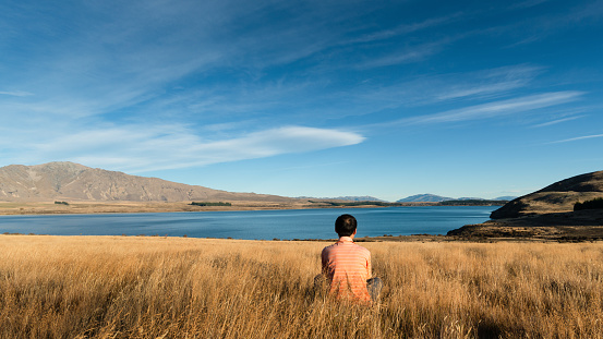 Man sitting on the long grass and enjoying views of Lake Tekapo from Peninsula walkway, South Island.