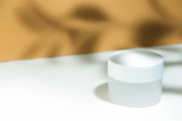 istock Empty white cosmetic jar container on a white beige background in the rays of the sun, with hard shadows from the razheniya. Cosmetology or skin care concept. Autumn cosmetics. Copy space 1343474703