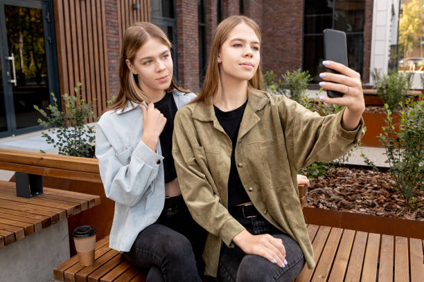 istock Pretty teenage twins making selfie while sitting on bench 1343474829