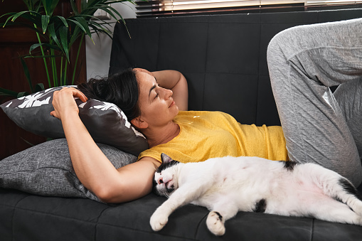 Woman and her cat are resting on the sofa. People on the couch.
