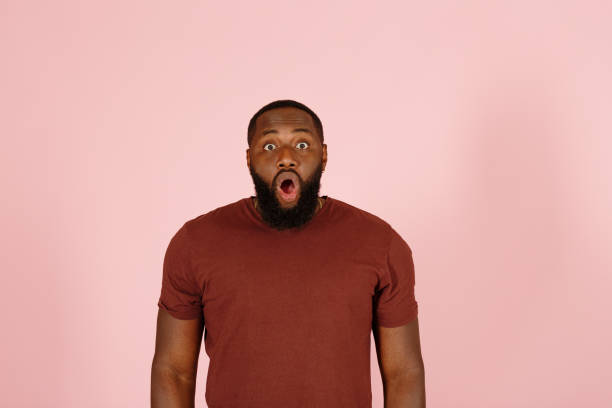 Funny shocked African-American guy actor on pink background stock photo