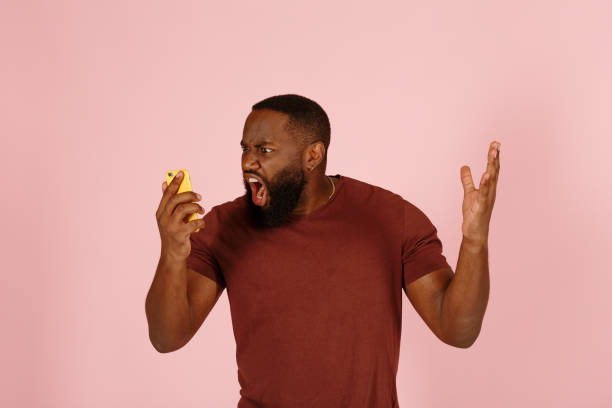 Angry African-American man screams holding phone on pink stock photo