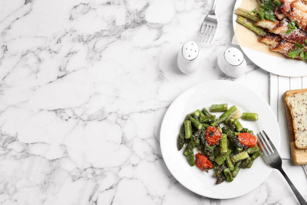 istock Dishes with oven baked asparagus served on white marble table, flat lay. Space for text 1343478735