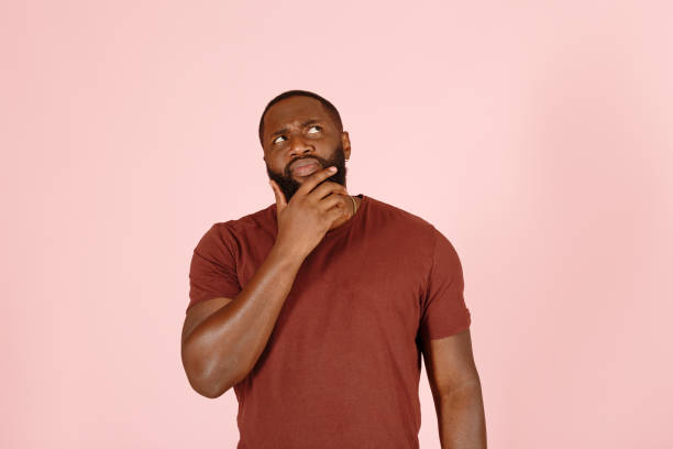 Thoughtful Afro-American person touches beard on pink stock photo