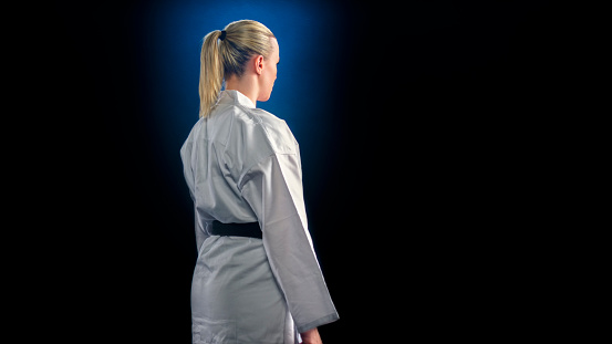 In motion. Male taekwondo fighter in white dobok, helmet and gloves training isolated over dark background. Concept of sport, education, skills, workout, health. Modern Korean martial art. Copy space for ad