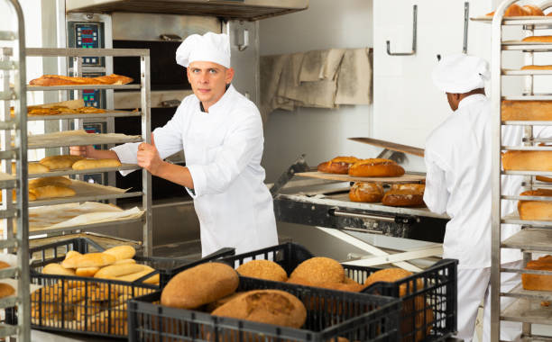istock Male baker carrying rack trolley with bread 1343484217
