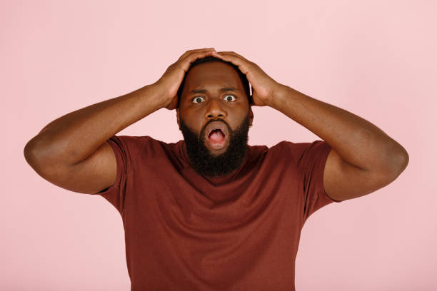 istock Sad shocked African-American man holds head on pink 1343486482