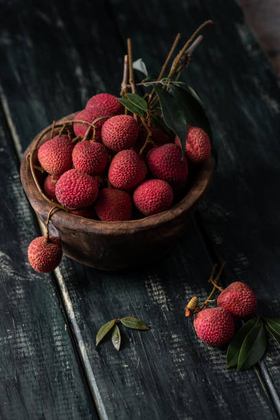 litchi se coloca en un plato de madera, pelado o sin abrir, sobre una mesa de grano de madera oscura - lichi fotografías e imágenes de stock