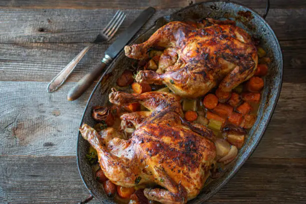 Homemade fresh cooked roasted chicken made with root vegetables and served in a rustic casserole dish on wooden table. Top view and closeup with copy space