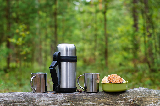 A picnic in the woods on a strom log. Thermos, two mugs and cookies on a log. Horizontal format.