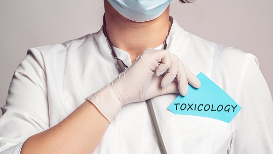 Cropped view of doctor in a white coat and sterile gloves holding a note with text - Toxicology. Medical concept