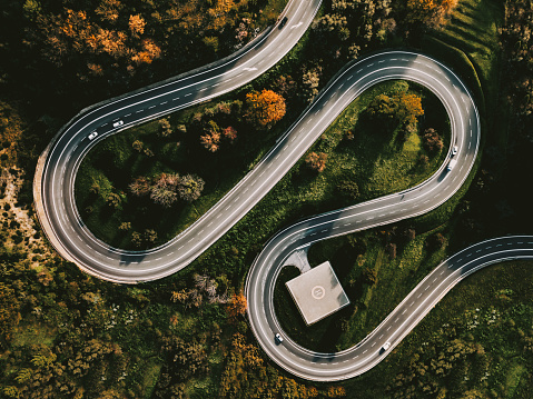 Aerial view of winding curved road with helipad and colourful autumn foliage in Italy countryside