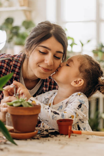 heureuse famille métaite, une jeune femme avec sa fille plante des plantes d’intérieur à la maison. jardinage à domicile. loisirs en famille, concept de passe-temps. conception de la biophilie et concept de jungle urbaine - mother family vertical flower photos et images de collection