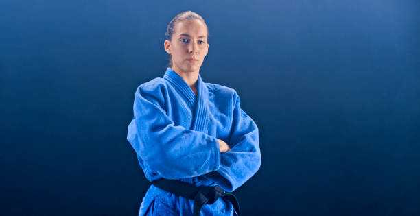Female judo player with arms crossed Portrait of female judo player with arms crossed standing against blue background. judo photos stock pictures, royalty-free photos & images