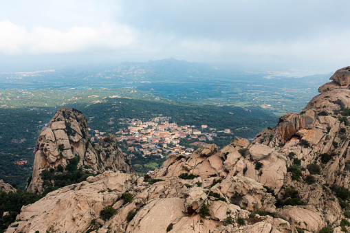View from above, drone point of view, stunning aerial landscape with a granite mountain in the foreground and San Pantaleo village in the distance during a cloudy day. Sardinia, Italy.