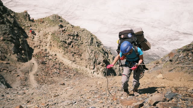 A climber with a large backpack with gear descends from the mountain on a rope using a belay system.