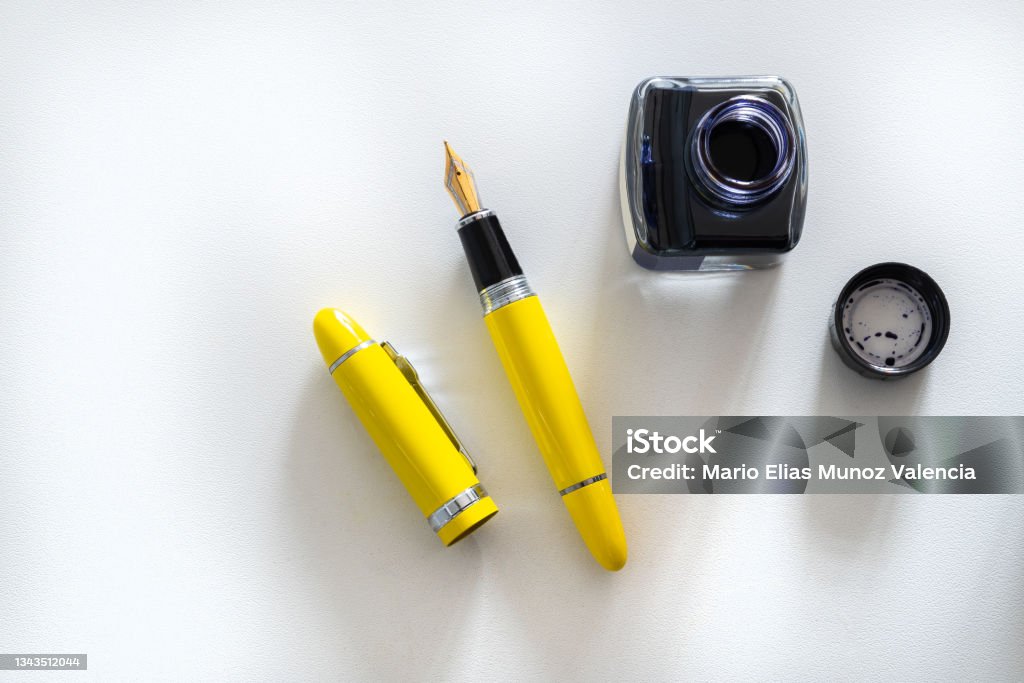 A yellow and black fountain pen next to a ink inkwell A yellow and black fountain pen next to a blue ink inkwell with copy space. Ink Well Stock Photo