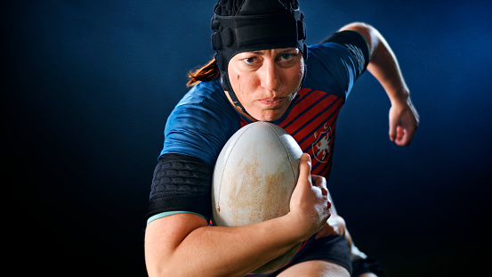 Close-up of female rugby player running with ball.