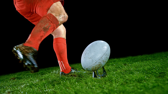 Low section of male rugby player kicking ball on field.