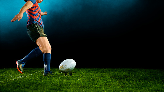 Low section of female rugby player kicking ball on field.