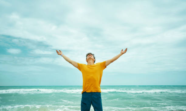 istock Inspired man enjoying majestic seascape while looking up and raised hands 1343513571