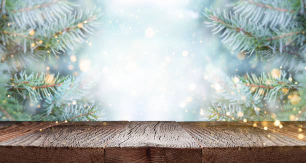 Empty wooden table top over branches of fir tree with snow and defocused lights.