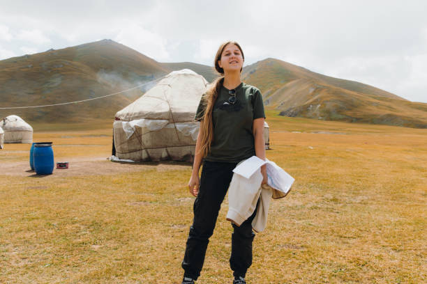 Woman traveler exploring the scenic mountain landscape with traditional yurts in Central Asia Smiling woman with long hair enjoying the morning at the mountain wilderness of Tian Shan, Staying near the old yurt yurt photos stock pictures, royalty-free photos & images