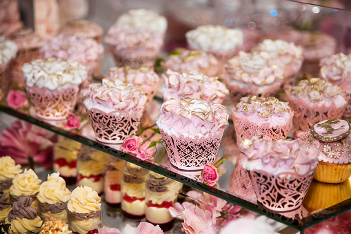 Delicious desserts at the wedding candy bar in the buffet area: muffins decorated with angels, sugar rosebuds and gold dye.