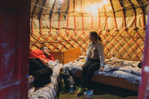 Young couple of backpackers relaxing in the small old yurt after the hiking trip in the campsite at Tian Shan, Kyrgyzstan