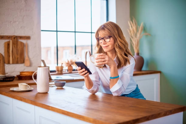 istock Smiling woman text messaging and drinking morning coffee while standing in the kitchen at home 1343517665