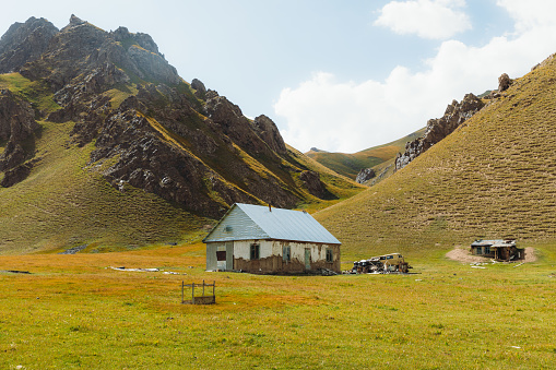 Summer sunny day in the wilderness of Kyrgyzstan, view of the old abandoned farm house and green peaks