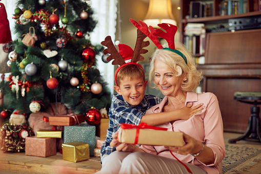 Happy senior woman surprising her grandson with present on Christmas day at home.