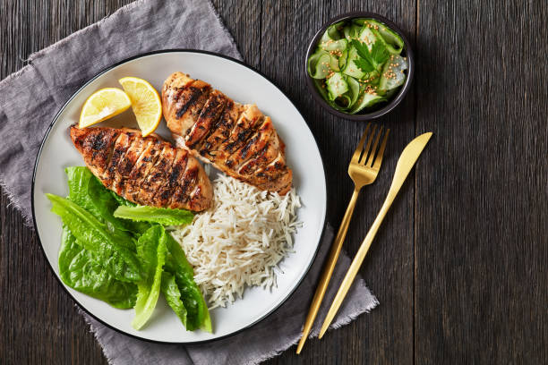 juicy grilled chicken breasts with fresh romaine lettuce leaves and rice on a plate on a dark wooden table, flat lay, free space stock photo