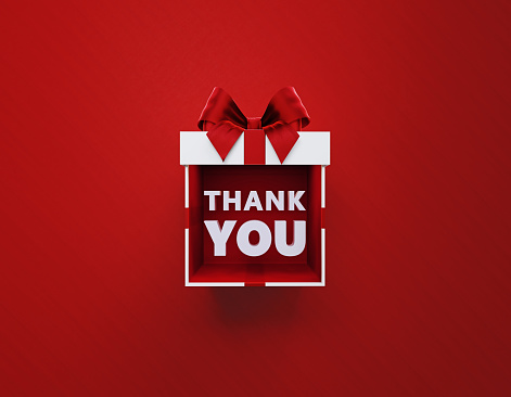 Thank you message sitting inside of a white gift box tied by heart shaped and thank you printed red ribbon sitting over red background. Horizontal composition with copy space. Directly above. Great use for Christmas, Mother's Day, birthday and Valentine's Day related gift concepts.