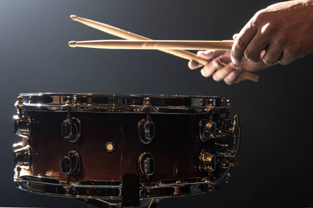 Snare drum and drummer's hands hitting drumsticks against a dark background. A man plays with sticks on a drum, a drummer plays a percussion instrument, copy space. percussion instrument stock pictures, royalty-free photos & images