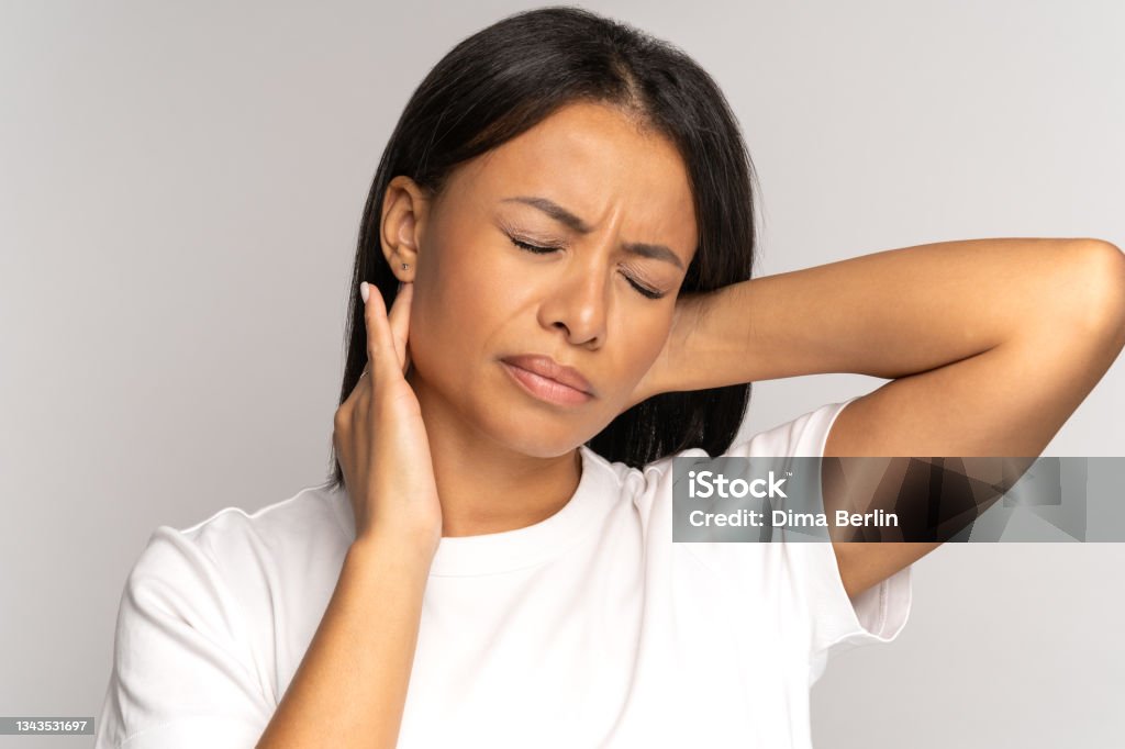 Tired african girl suffer from neck pain, spinal problem, incorrect posture, fibromyalgia. Neck ache Tired girl suffer from neck pain, pinched nerve in her back. African woman has spinal problem, muscle inflammation, rheumatoid pain isolated on studio grey background. incorrect posture, fibromyalgia. Chronic Illness Stock Photo