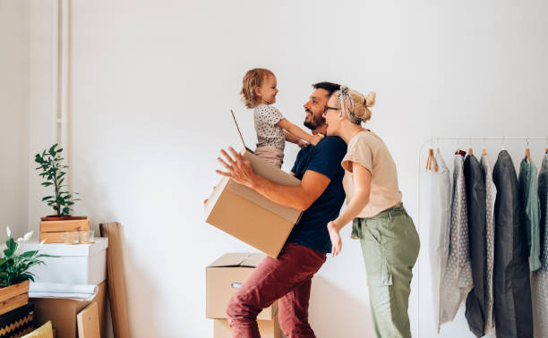 Cheerful Family Moving In New Home Happy family with one child having fun while carrying and unpacking boxes in new home on moving day new home stock pictures, royalty-free photos & images