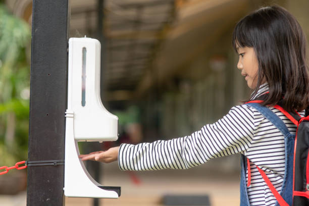 istock Child girls kid using automatic alcohol gel dispenser spraying on hands sanitizer machine antiseptic disinfectant, new normal life after Coronavirus COVID-19 pandemia. 1343539621