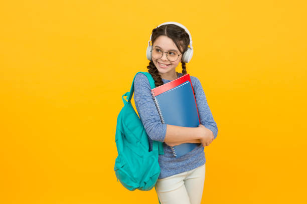 ragazza studentessa moderna con zaino e materiale scolastico sfondo giallo, concetto di lezioni audio - home schooling audio foto e immagini stock