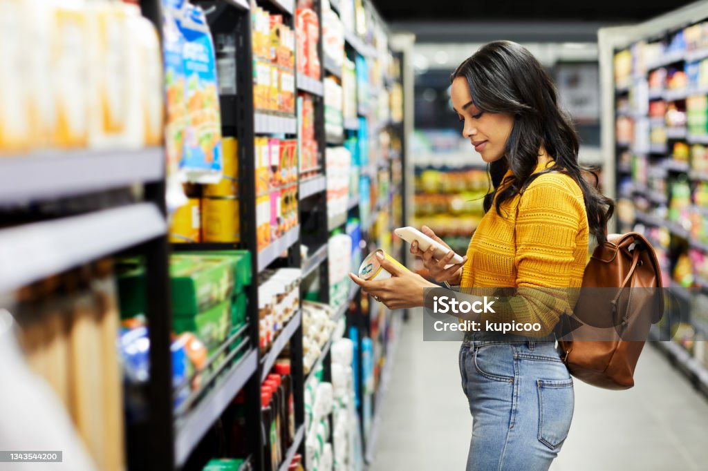 Shot of a young woman shopping for groceries in a supermarket When the going gets tough, the tough eats Cherry Supermarket Stock Photo