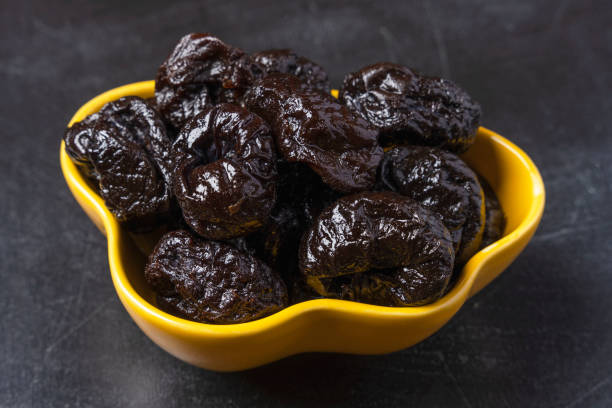 Sweet delicious prunes in a yellow plate on a black background. Delicious natural delicacy, dessert stock photo