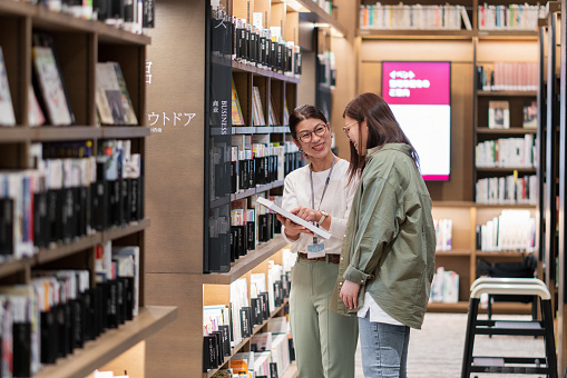 Staff in a library helping a customer to find a book. Okayama, Japan