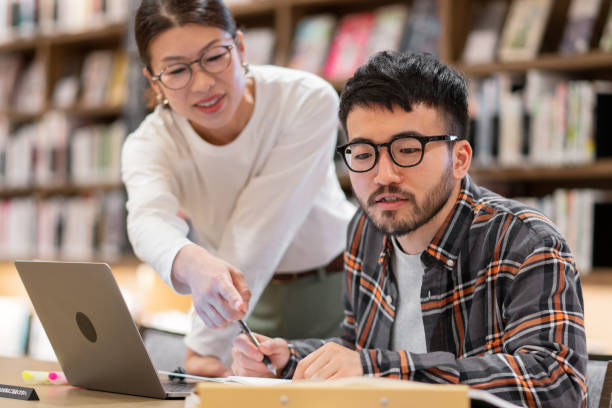 professor im gespräch mit einem studenten in einer bibliothek - professor stock-fotos und bilder