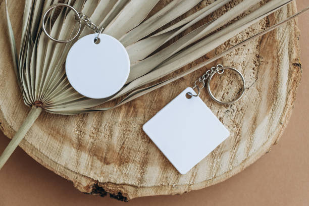 Keychain mockup among brown palm leaves to display design. Blank white sublimation key chain photo.
