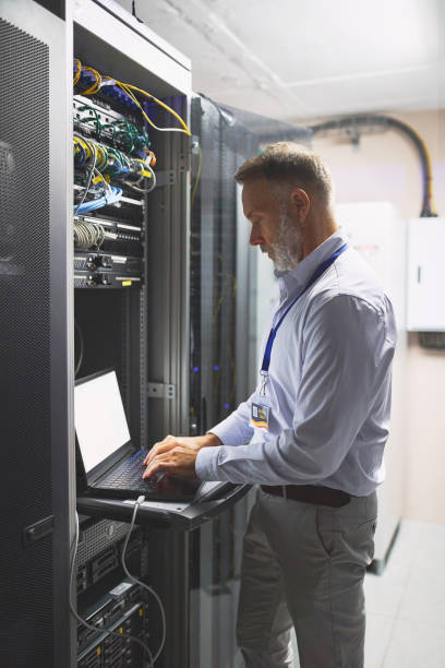 istock Shot of a mature man using a laptop while working in a server room 1343548822