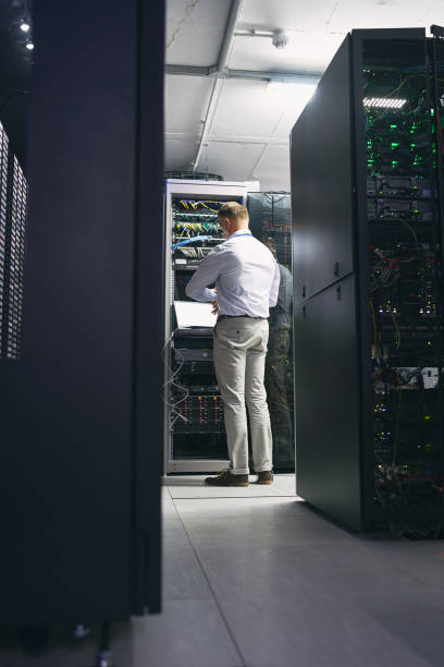 istock Rearview shot of a mature man using a laptop while working in a server room 1343549353