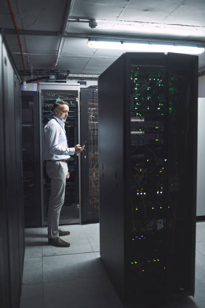 istock Shot of a mature man using a cellphone while working in a server room 1343550811