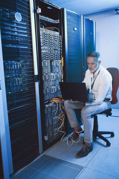 istock Shot of a mature man using a laptop while working in a server room 1343550833