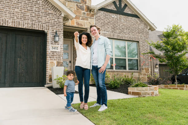 Family proudly displays house key after purchasing home The young family stands in the front yard and proudly displays the keys to their new home. happy family with key of their new house stock pictures, royalty-free photos & images